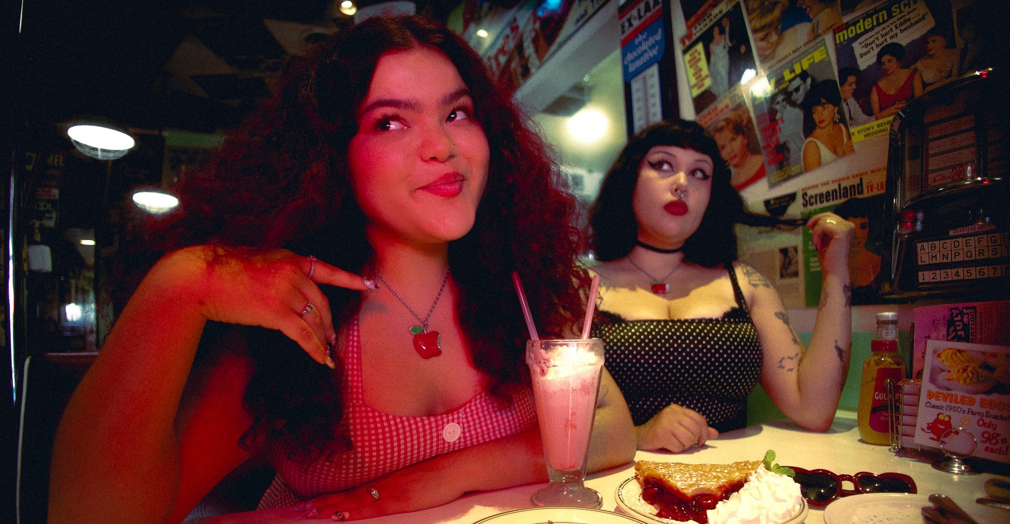 Two women sitting at a table with desserts in a retro-themed restaurant.